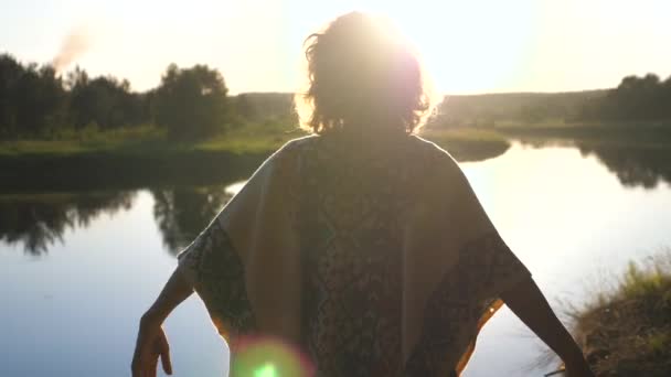 Mladá šťastná žena zvedá ruce při západu slunce na břehu řeky — Stock video