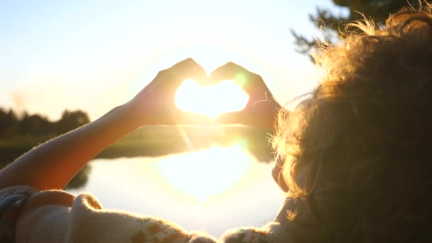 Mulher mãos formando um coração ao pôr do sol sobre o rio — Vídeo de Stock