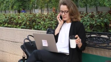 Laptop 'u kahve molasında olan iş kadını akıllı telefondan konuşuyor.