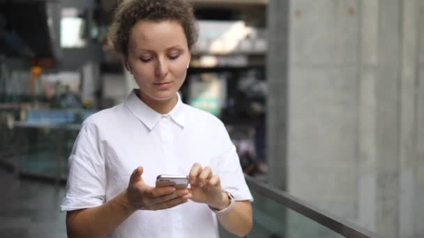 Młoda kobieta w Airpods i Smartwatch za pomocą smartfona w mieście — Wideo stockowe