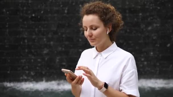Σύγχρονη γυναίκα στους αεροθαλάμους και Smartwatch χρησιμοποιώντας Smartphone στην πόλη — Αρχείο Βίντεο