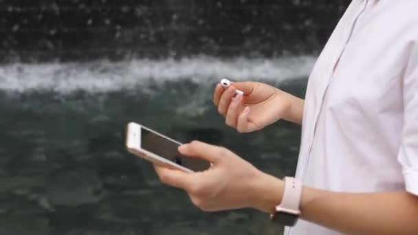 Женские руки соединяют наушники AirPods со смартфоном и умными часами — стоковое видео