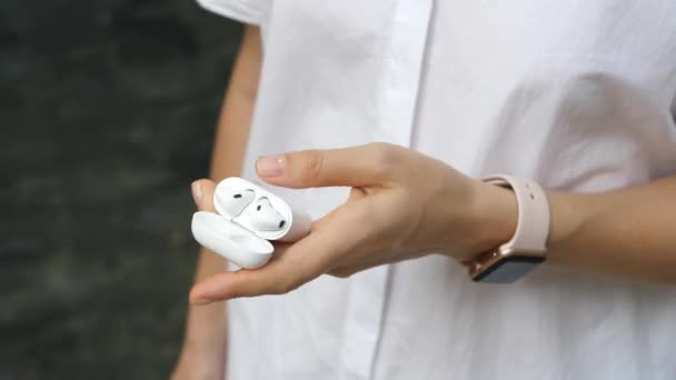 Mano en Smartwatch celebración de auriculares inalámbricos Bluetooth con caja de carga — Vídeos de Stock