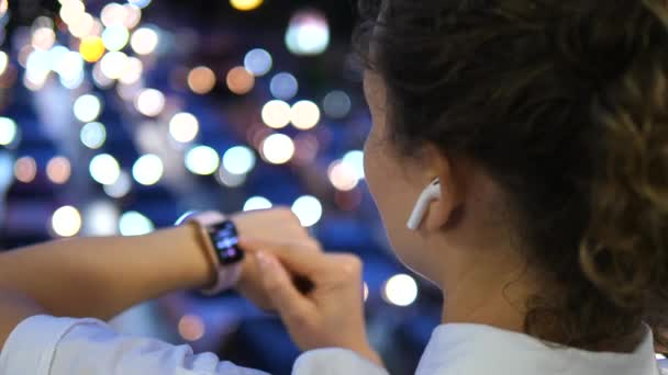 Vrouw in draadloze oortelefoons met behulp van Smartwatch In Night City — Stockvideo