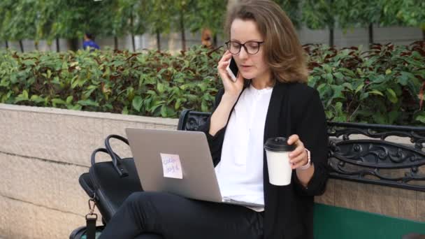 Femme d'affaires avec ordinateur portable sur pause café parlant sur Smartphone — Video