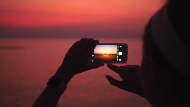 Mains féminines prenant des photos avec téléphone portable du coucher du soleil sur la mer — Video