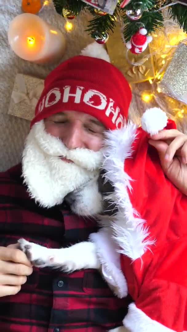 Unge man kramar sin hund i Santa Costumes. Julfirande. — Stockvideo