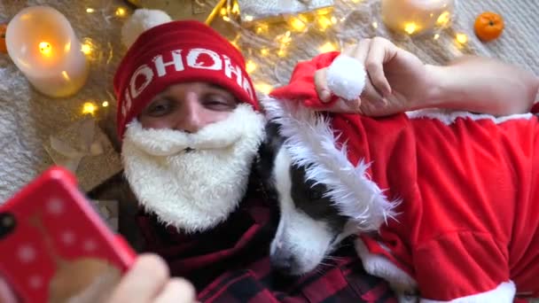 Mladý muž v santa kostým přičemž vánoční selfie se psem — Stock video