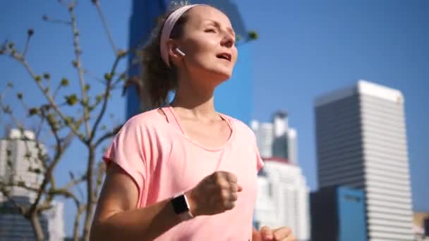 スマートウォッチと無線イヤホンを着て公園で走っているスポーツ女性 — ストック動画