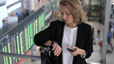İş kadını cep telefonu kullanıyor ve havaalanındaki Smartwatch saatini kontrol ediyor..