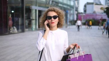 Genç bayan alışveriş merkezi yakınında telefonla konuşuyor.