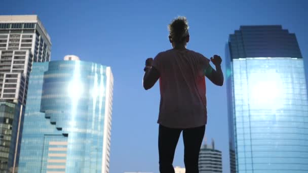 Ganadora fuerte y confiada levantando armas al cielo contra el fondo de la ciudad — Vídeo de stock