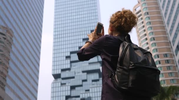 Жінка подорожує з рюкзаком, фотографуючи місто з мобільним телефоном. — стокове відео