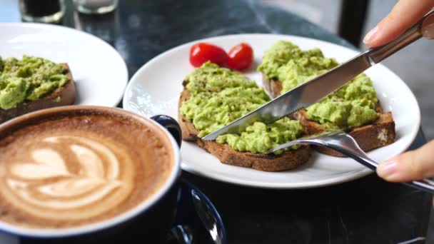 女性の手はコーヒーと朝食を持ちながらアボカドトーストをカット — ストック動画