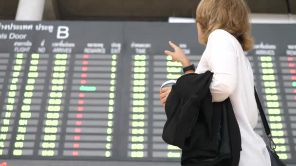 Mulher de negócios com café para ir no aeroporto à procura de voo na placa cronometrável — Vídeo de Stock