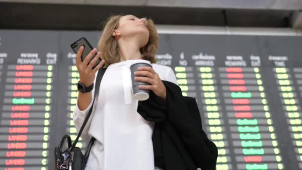 Junge Geschäftsfrau nutzt Smartphone bei der Fahrplananzeige am Flughafen — Stockvideo