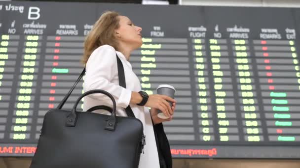 Ung affärskvinna med kaffe väntar på flygplatsen flyg avgång skärm — Stockvideo