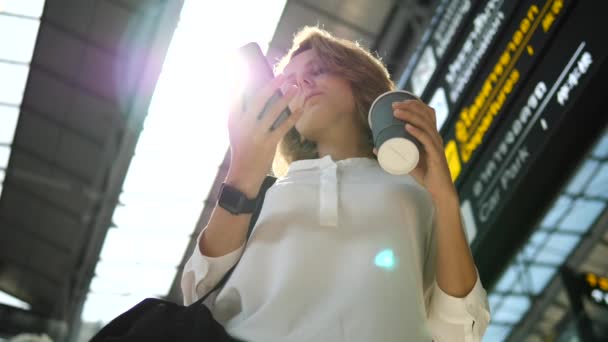 Zakelijke vrouw met smartwatch op de hand en koffie met behulp van mobiele telefoon in de luchthaven — Stockvideo