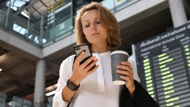 Jonge zakenvrouw met koffie met behulp van Smartphone op de luchthaven vlucht Dienstregeling — Stockvideo