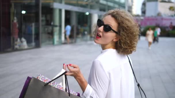Ευτυχισμένη γυναίκα με γυαλιά ηλίου Περπατώντας με τσάντες ψώνια Έξω — Αρχείο Βίντεο