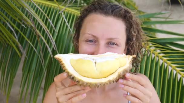 Glada unga kvinna äta Durian på en strand — Stockvideo