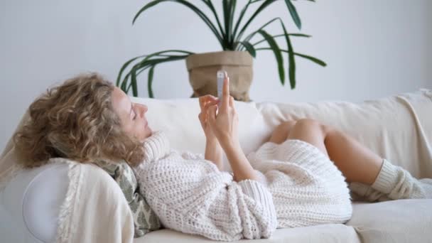 Γυναίκα ξαπλωμένη στον καναπέ και χρησιμοποιώντας το κινητό τηλέφωνο — Αρχείο Βίντεο