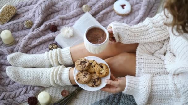 Mujeres manos y pies en suéter y punto acogedor calcetines beige sosteniendo taza de chocolate caliente y galletas — Vídeos de Stock