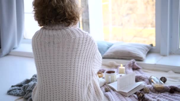 Jeune femme en pull tricoté chaud à la maison regardant la fenêtre — Video