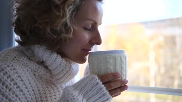 Mujer joven en jersey de punto oliendo té o aroma de café por la ventana — Vídeos de Stock