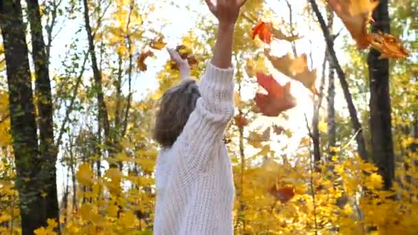 Une jeune femme excitée jette des feuilles d'automne dans le parc 