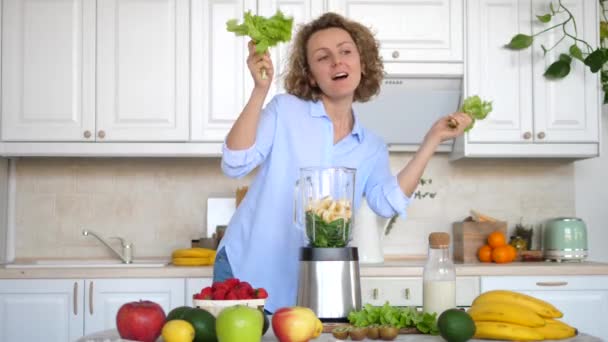 Gesunder, glücklicher Lebensstil. Frau tanzt in Küche mit Salat und bereitet Smoothie zu. — Stockvideo