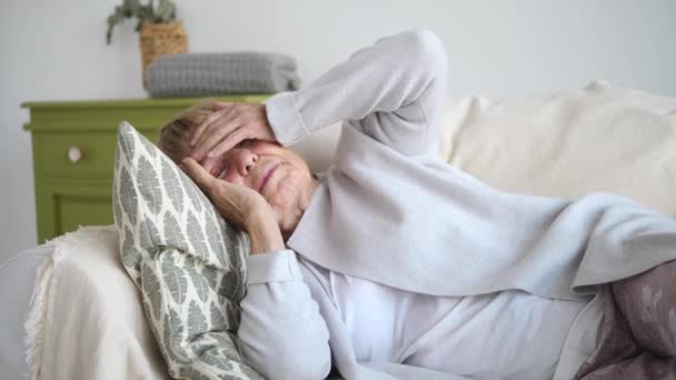 Старуха страдает от головной боли, лежащей на диване — стоковое видео