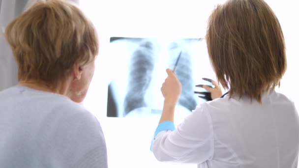 Доктор показывает рентген старшему пациенту в медицинском кабинете — стоковое видео