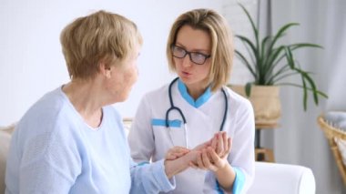 Ev ziyareti sırasında yaşlı hastanın nabzını ölçen kadın doktor..