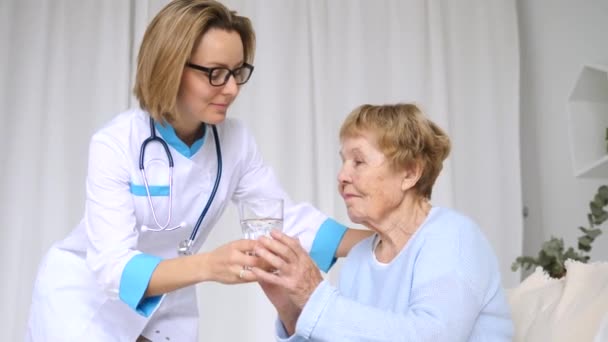 Médico amamantando a una mujer mayor dándole un vaso de agua — Vídeo de stock