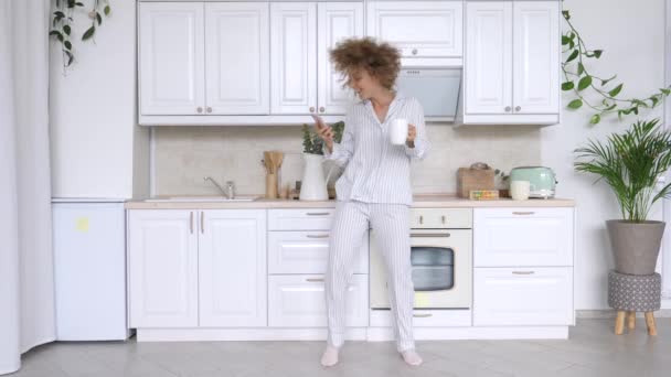 Concepto de gente y tecnología. Mujer feliz con teléfono inteligente, bailando y sonriendo en la cocina — Vídeos de Stock