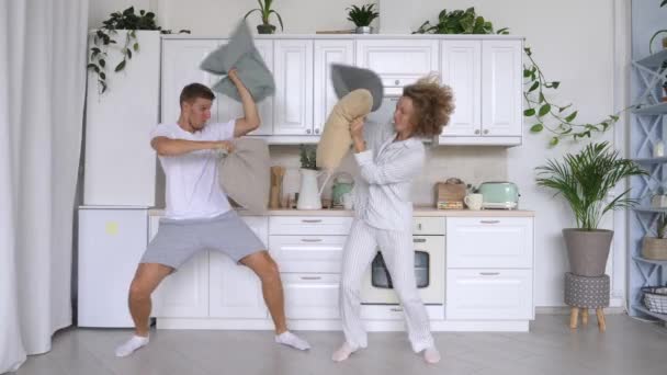 Pareja divertida luchando con almohadas en la cocina — Vídeos de Stock