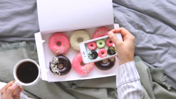 Kadın Elleri, yatakta kahvaltıda akıllı donutlarla yemek fotoğrafı çekiyor. — Stok video