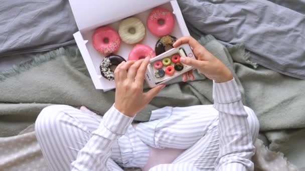 Yatakta cep telefonlu donutların fotoğrafını çeken kadın. — Stok video