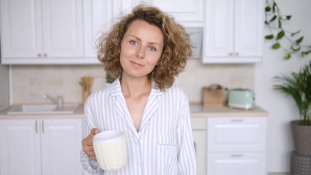 Vrouw in pyjama staan met kopje thee op keuken in de ochtend — Stockvideo