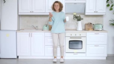 Genç Kadın Mutfakta Dans Ediyor ve Akıllı Telefon Kullanıyor