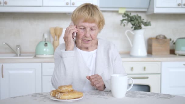 Büyükanne arıyor, akıllı telefondan arıyor ve mutfakta konuşuyor. — Stok video