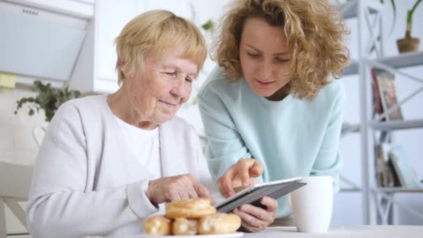 Внучка помогает бабушке с планшетным компьютером дома — стоковое видео