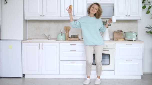 Giovane donna che balla nella cucina bianca al mattino con caffè e ciambella — Video Stock