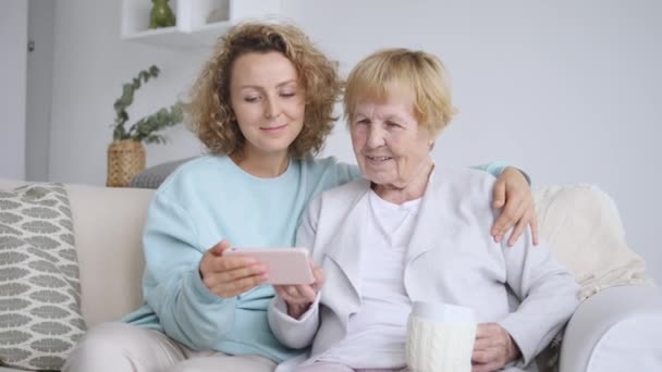 Barnbarn och mormor med mobiltelefon inomhus — Stockvideo