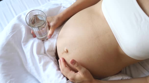 Hydratatie tijdens de zwangerschap. Sluiten van zwangere vrouw buik en glas water. — Stockvideo