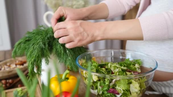 Zwangere vrouw toevoegen van verse kruiden aan gezonde veganistische salade koken op keuken. — Stockvideo