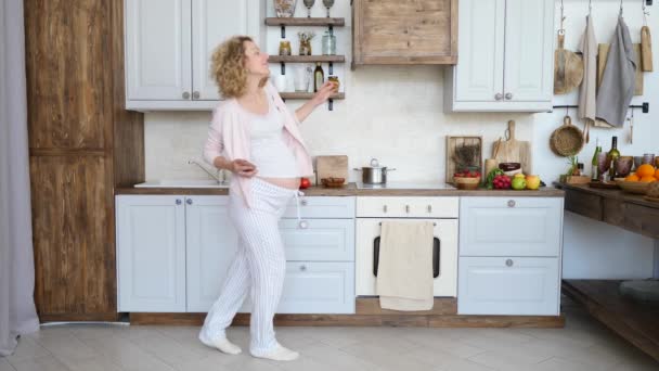 Vrolijke zwangere vrouw dansen met mobiele telefoon in handen op keuken. — Stockvideo