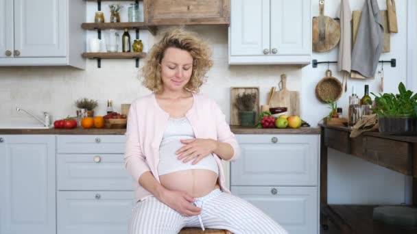 Gelukkig zwanger vrouw zitten op stoel en aanraken van haar buik thuis — Stockvideo
