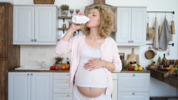 Zwangere jonge vrouw drinken yoghurt in de keuken. — Stockvideo